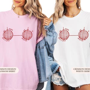May include: Two t-shirts, one pink and one white, with a red disco ball graphic. Text reads "2025", "Olivia's Bach", and "Nashville". The pink shirt is labelled "Crimson Design Blossom Shirt", and the white shirt is labelled "Crimson Design White Shirt".
