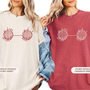 May include: Two t-shirts, one cream and one crimson, each with a red graphic of two disco balls linked by a line. The text above the left disco ball reads "2023", and below the disco balls are the words "Olivia's Bash" and "Nashville".