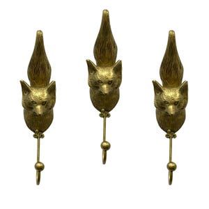 May include: A set of three gold-toned metal wall hooks, each featuring a sculpted fox head with a textured tail extending upward and a slender hook extending downward from the chin, secured by two small visible screws at the base of the head.