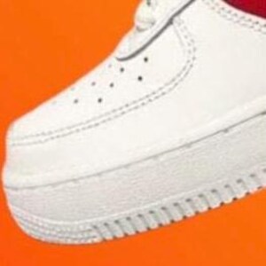Puede incluir: Primer plano del dedo del pie de cuero blanco de una zapatilla blanca y roja. La suela es blanca con un patr&oacute;n texturizado.