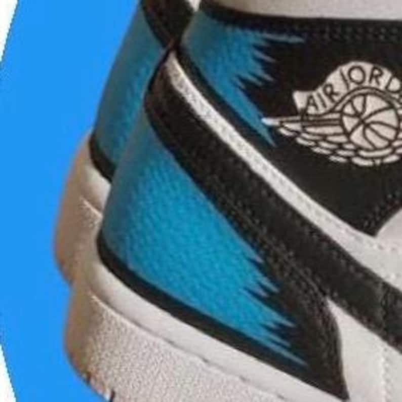 May include: Close-up of a white and black Air Jordan sneaker with a light blue accent on the side. The shoe features the Air Jordan logo and a white sole.