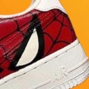 Puede incluir: Zapatillas blancas de cuero con un dise&ntilde;o de Spiderman rojo y negro pintado en el lateral.