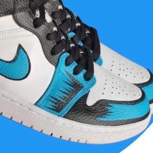 May include: Pair of high-top sneakers in white, black, and blue. The sneakers feature a white base with blue accents on the side and toe, black laces, and a black and gray collar. The sole is white.