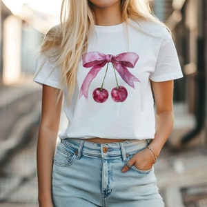 Puede incluir: Camiseta blanca con un lazo rosa de acuarela y dos cerezas colgando del lazo.