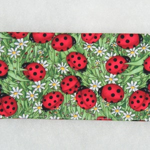 May include: A red and black ladybug print fabric wallet with a green background and white daisy flowers.
