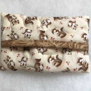 May include: A beige quilted tissue box cover with a brown trim. The cover features a repeating pattern of brown squirrels and red berries.