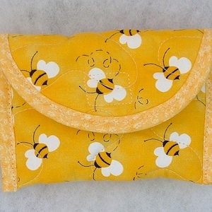 Puede incluir: Una bolsa de tela amarilla con cierre de cremallera y un patr&oacute;n de abejas. La bolsa est&aacute; forrada con tela amarilla y tiene un ribete blanco.