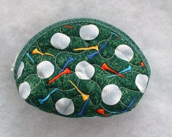 Può includere: Una pochette con cerniera in tessuto verde con un design di palline da golf e tee. La pochette è trapuntata e ha un tiretto della cerniera bianco.