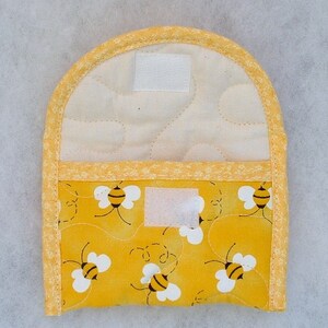 Puede incluir: Manopla de cocina acolchada amarilla con un patr&oacute;n de abejas. La manopla tiene un forro de tela blanca y un ribete amarillo. Tiene dos cierres de velcro blancos.