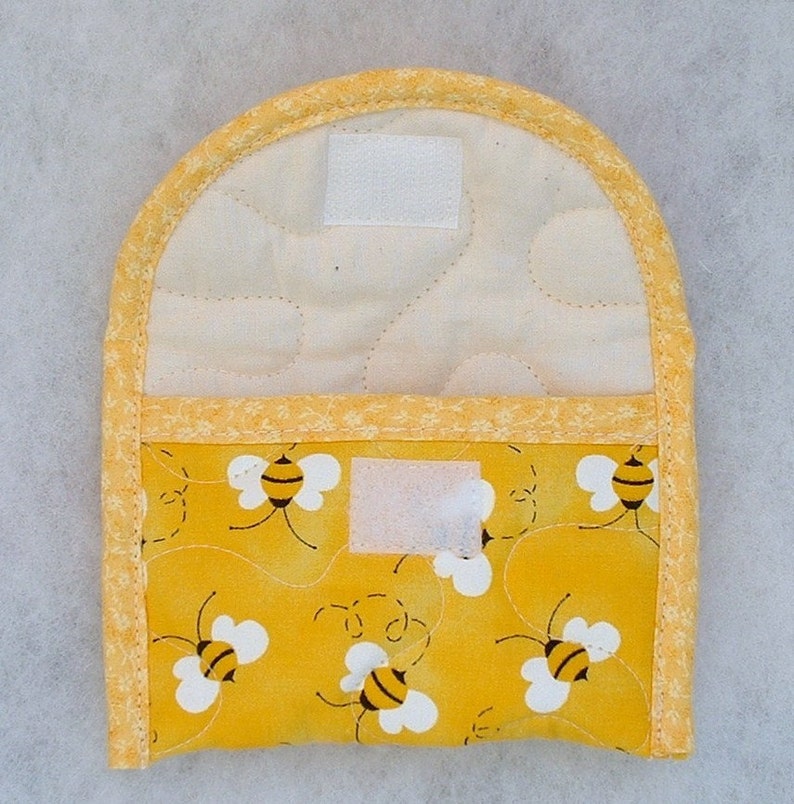 Puede incluir: Manopla de cocina acolchada amarilla con un patr&oacute;n de abejas. La manopla tiene un forro de tela blanca y un ribete amarillo. Tiene dos cierres de velcro blancos.