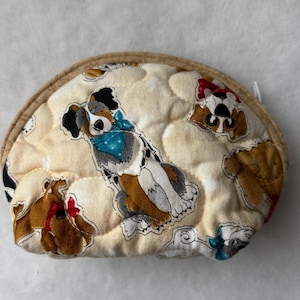 May include: A quilted, round coin purse with a beige background and a repeating pattern of cartoon dogs. The dogs are in various colors, including brown, black, and white, and some are wearing bandanas. The purse has a tan border.