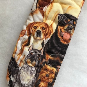May include: Quilted oven mitt featuring a collage of various dog breeds. The mitt showcases a Beagle, Rottweiler, Schnauzer, and Yorkshire Terrier, among others. The top edge is trimmed with a brown fabric.