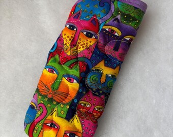Könnte beinhalten: Ein gestepptes Brillenetui aus Stoff mit einem lebendigen, mehrfarbigen Muster aus stilisierten Katzengesichtern in den Farben Pink, Orange, Gelb, Grün, Blau und Violett. Das rechteckige Etui hat eine abgerundete Oberkante und sichtbare Nähte.