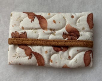 Könnte beinhalten: Ein gesteppter Kartenhalter mit einem sich wiederholenden Muster aus braunen Eichhörnchen, Blättern und Eicheln auf cremefarbenem Hintergrund. Der Kartenhalter hat ein braunes Stoffband in der Mitte.