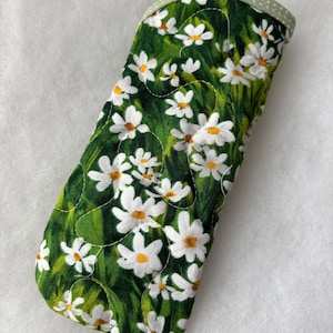 以下が含まれることがあります： 白いヒナギクと黄色の中心部が特徴の、緑色の花柄のキルティングメガネケース。ケースは丸みを帯びた上部と、薄い緑色の水玉模様のトリムが付いています。長さ約17cm。