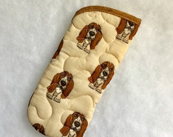 Puede incluir: Una manopla de horno acolchada beige con ribete marrón presenta un patrón repetido de caras de perros basset.