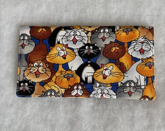Puede incluir: Una funda de talonario rectangular con un patrón repetido de gatos de dibujos animados en naranja, marrón, negro y gris. Los gatos tienen expresiones exageradas y están sobre un fondo azul y gris.