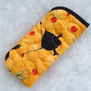 May include: A quilted oven mitt with a black bird design and red cherries on a yellow background.