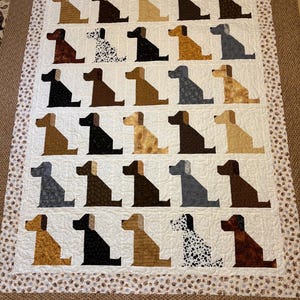 May include: A rectangular quilt featuring a grid of thirty stylized dog silhouettes in various shades of brown, black, gray, and white, including spotted patterns. The quilt has a white background with swirling quilting and a paw print border.
