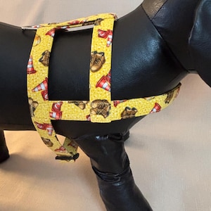 Op de afbeelding: Gele hondentuig met een bouwthema. Het tuigje heeft een herhalend patroon van oranje verkeerskegels en bruine werkschoenen. Het tuigje is ontworpen om rond de borst en rug van de hond te passen.