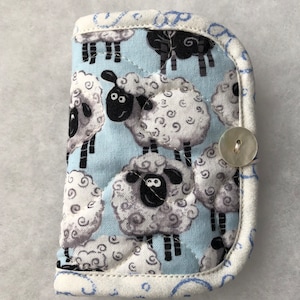 May include: A blue quilted fabric hot pad with a white and black sheep pattern. The hot pad has a white button on the side.
