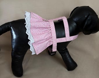 Könnte beinhalten: Ein rosa Hundegeschirr mit weißem Tupfenmuster und einem Rüschenrock. Das Geschirr hat weiße Spitzentrimm und ein passendes rosa Riemendesign. Das Hundegeschirr ist für einen kleinen Hund konzipiert.