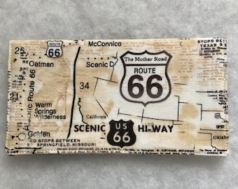 Könnte beinhalten: Eine Vintage-Stoffkarte der Route 66 mit einem schwarz-weißen Schild mit dem Text "The Mother Road ROUTE 66" und dem Text "US 66 HI-WAY" darunter. Die Karte enthält auch den Text "Historic Route 66", "Scenic D", "California", "Warm Springs Wilderness", "Gökten", "Oatman", "McConnico" und "SED STOPS BETWEEN SPRINGFIELD, MISSOURI".