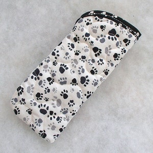 May include: A white quilted oven mitt with a black paw print pattern. The mitt has a black trim around the edges.