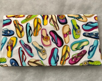 Può includere: Un portafoglio in tessuto bianco con una stampa colorata di infradito. Le infradito sono di vari colori, tra cui blu, verde, giallo, rosa e rosso.