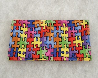 Könnte beinhalten: Eine farbenfrohe Stoffbörse mit einem Puzzle-Muster. Die Börse ist aus weichem, strapazierfähigem Stoff gefertigt und verfügt über einen Reißverschluss.