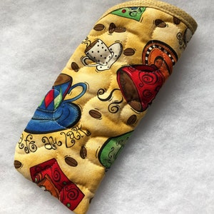 May include: A yellow quilted oven mitt with a coffee cup and coffee bean design. The mitt has the text "Cafe au Lait" on it.