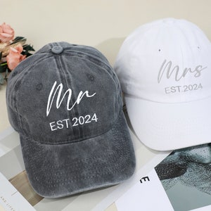 May include: Two baseball caps, one grey and one white, with the words "Mr. EST. 2024" and "Mrs. EST. 2024" embroidered on them.