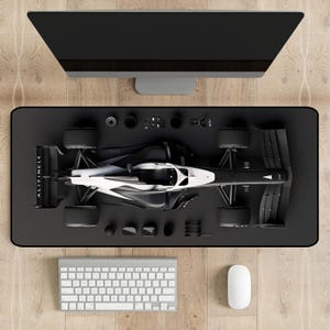 May include: A black and white race car model on a black desk mat with the word "ALITINEK" printed on the side. The car is surrounded by small black and silver parts.