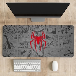 May include: Gray rectangular mouse pad featuring a comic book style design with Spider-Man illustrations. A large red Spider-Man emblem is centered on the pad. A keyboard, mouse, and computer monitor are visible.