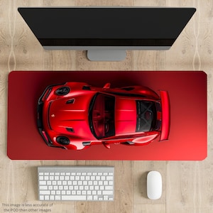 May include: A red Porsche 911 GT3 RS sports car viewed from directly above. The car is on a red desk mat with a computer monitor, keyboard, and mouse in the background.