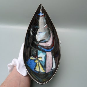 May include: A black ceramic serving dish with a teardrop shape. The dish is decorated with a colorful abstract design in shades of blue, pink, yellow, and white.