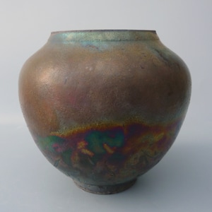 May include: A round, brown ceramic vase with a metallic glaze. The glaze has a rainbow effect, with shades of green, blue, and purple.