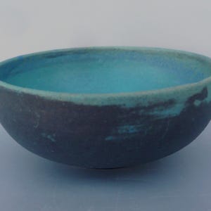 May include: A blue and black ceramic bowl with a textured surface. The bowl is empty and has a light blue glaze on the inside.