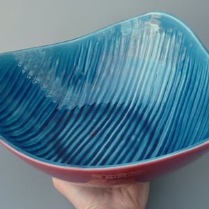 May include: A square ceramic bowl with a teal blue glaze and a red rim. The bowl has a textured, striped pattern.