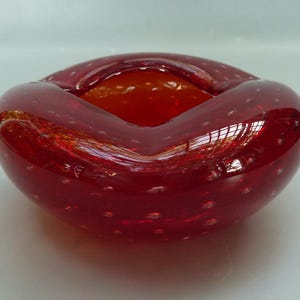 May include: A red glass ashtray with a bubbled texture and a rounded, heart-shaped design.