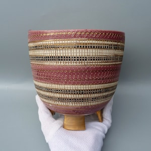 May include: A pink ceramic planter with gold and black geometric patterns and three short legs.