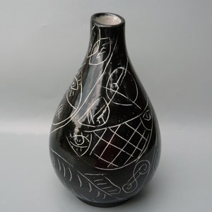 May include: Black ceramic vase with white abstract design. The design features geometric shapes, lines, and eyes.