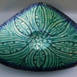 May include: A decorative, triangular-shaped ceramic bowl with a glossy finish. The bowl features a teal and blue color scheme with a floral pattern. The rim is a dark blue, and the interior has a textured, raised design.