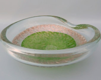 May include: A clear glass bowl with a green and pink iridescent design. The bowl has a wavy edge and a round, slightly indented center.