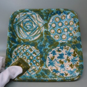 May include: Square ceramic tray with a blue and green abstract design. The tray has four sections, each with a different pattern. The tray is perfect for serving snacks or appetizers.