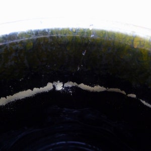 May include: Close-up of the inside of a ceramic pot, showing a dark black glaze with a thin white line around the rim. The glaze has a green tint.