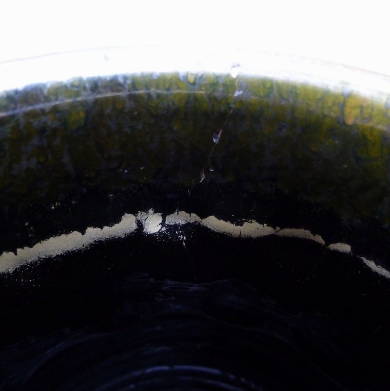 May include: Close-up of the inside of a ceramic pot, showing a dark black glaze with a thin white line around the rim. The glaze has a green tint.