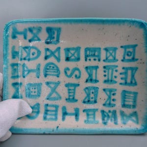 May include: A white ceramic rectangular dish with a turquoise blue border and a pattern of blue symbols on the surface.