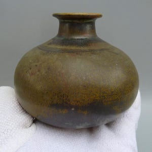 May include: A small, round, brown ceramic vase with a narrow neck. The vase has a mottled brown and green glaze.