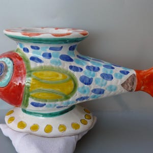 May include: A whimsical, hand-painted ceramic fish figurine. The fish features a red head, yellow and green midsection, and a bright orange tail. The body is white with blue polka dots. The fish is a decorative item.